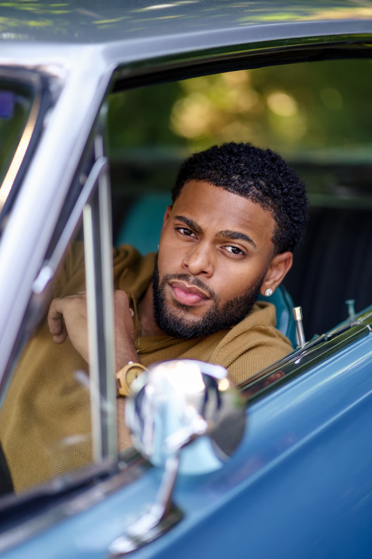Brandon Miles seated in a vintage blue car, photographed through the open window
